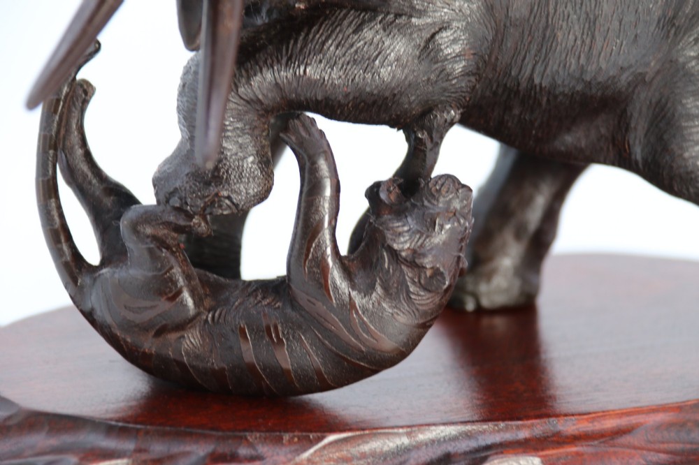 A dark patinated bronze sculpture of an elephant defending itself against two tigers, mounted on a carved wooden base. View XI