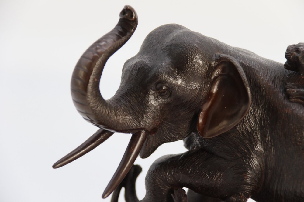 A dark patinated bronze sculpture of an elephant defending itself against two tigers, mounted on a carved wooden base. View XIII