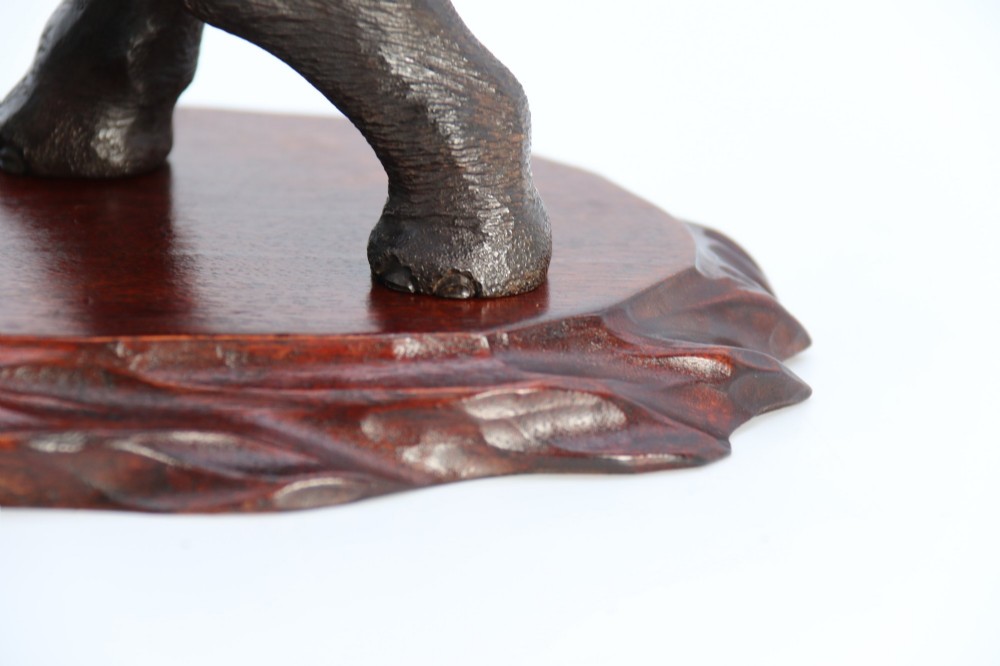 A dark patinated bronze sculpture of an elephant defending itself against two tigers, mounted on a carved wooden base. View XIV