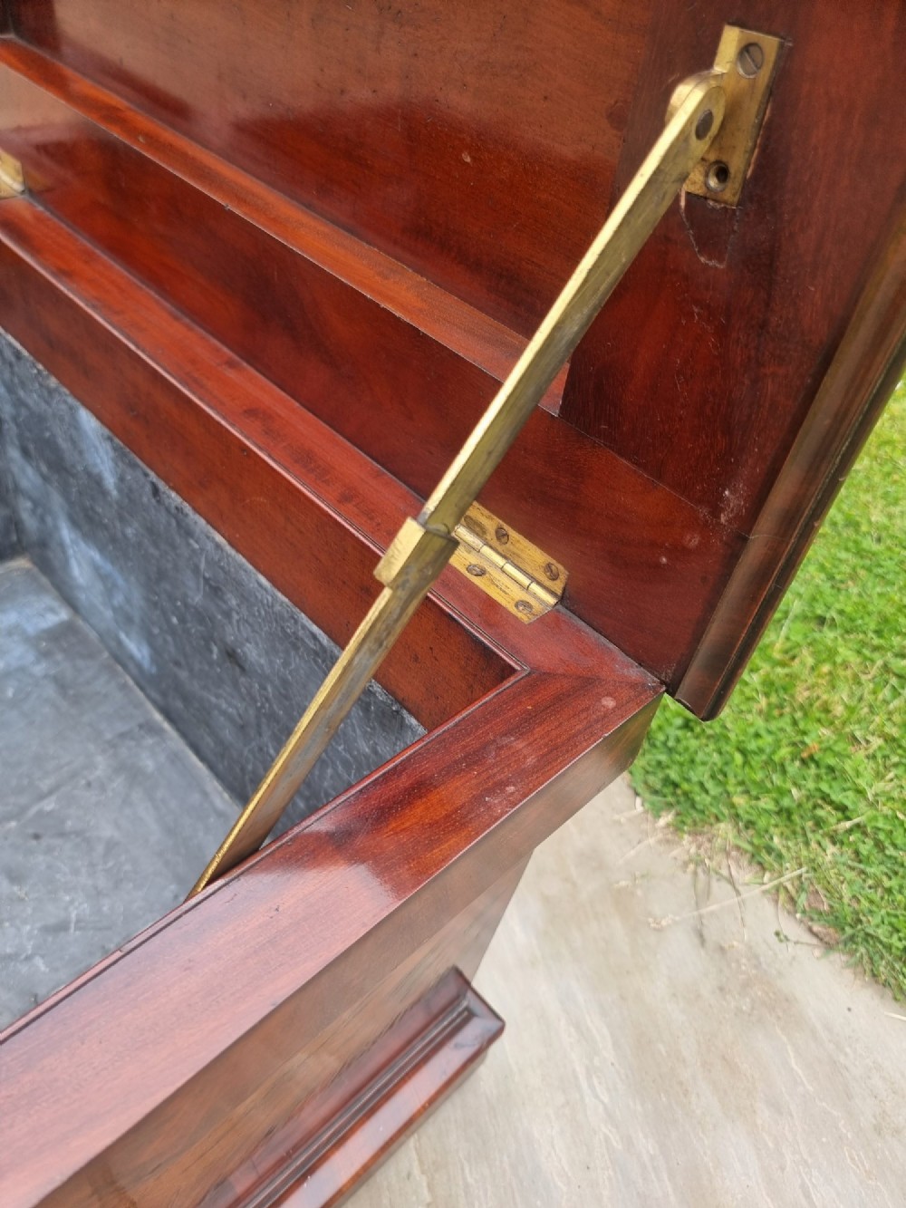 An antique Regency flame mahogany wine cooler in a tapered sarcophagus shape with a stepped hinged lid and a moulded plinth base. View VI
