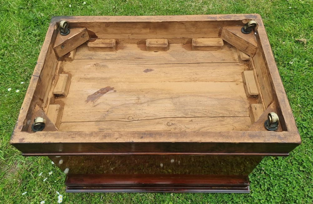 An antique Regency flame mahogany wine cooler in a tapered sarcophagus shape with a stepped hinged lid and a moulded plinth base. View X