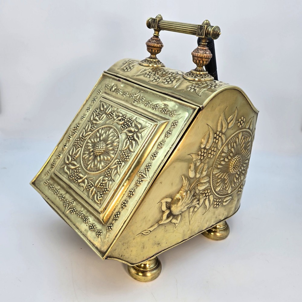 Victorian sloped brass coal box featuring repousse sunflower motifs, turned brass feet, and a top carrying handle with an integrated rear shovel. View III