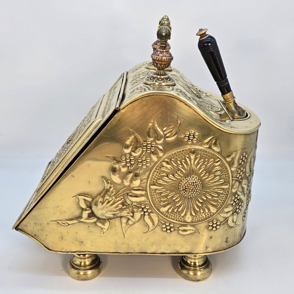 Victorian sloped brass coal box featuring repousse sunflower motifs, turned brass feet, and a top carrying handle with an integrated rear shovel. View IV