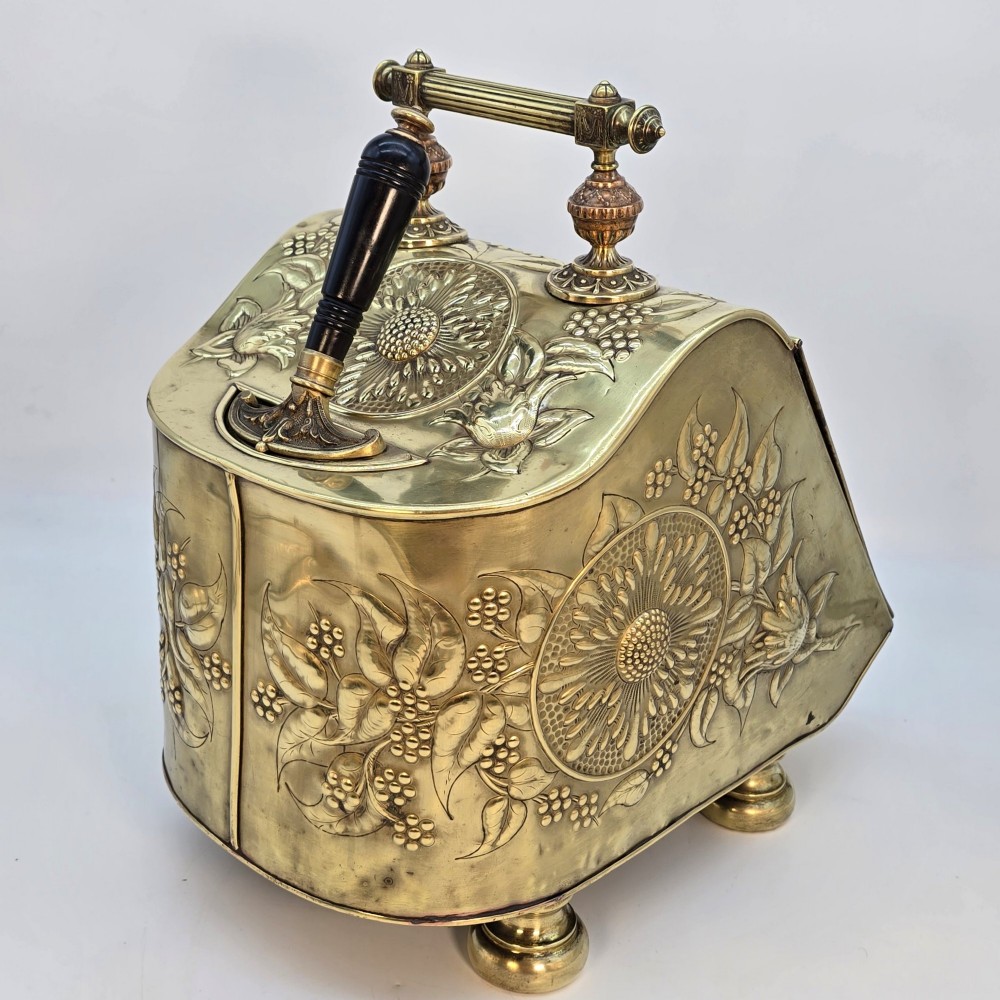 Victorian sloped brass coal box featuring repousse sunflower motifs, turned brass feet, and a top carrying handle with an integrated rear shovel. View VII
