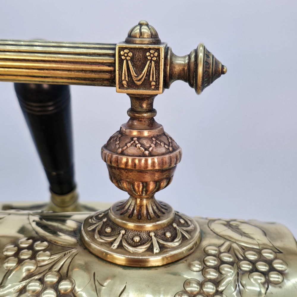 Victorian sloped brass coal box featuring repousse sunflower motifs, turned brass feet, and a top carrying handle with an integrated rear shovel. View X