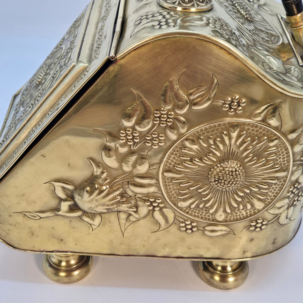 Victorian sloped brass coal box featuring repousse sunflower motifs, turned brass feet, and a top carrying handle with an integrated rear shovel. View XIV