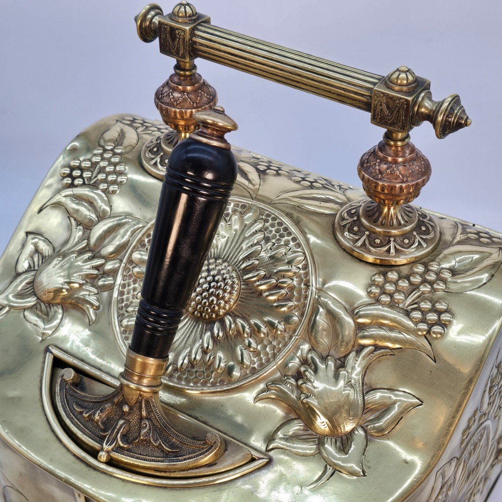Victorian sloped brass coal box featuring repousse sunflower motifs, turned brass feet, and a top carrying handle with an integrated rear shovel. View XV