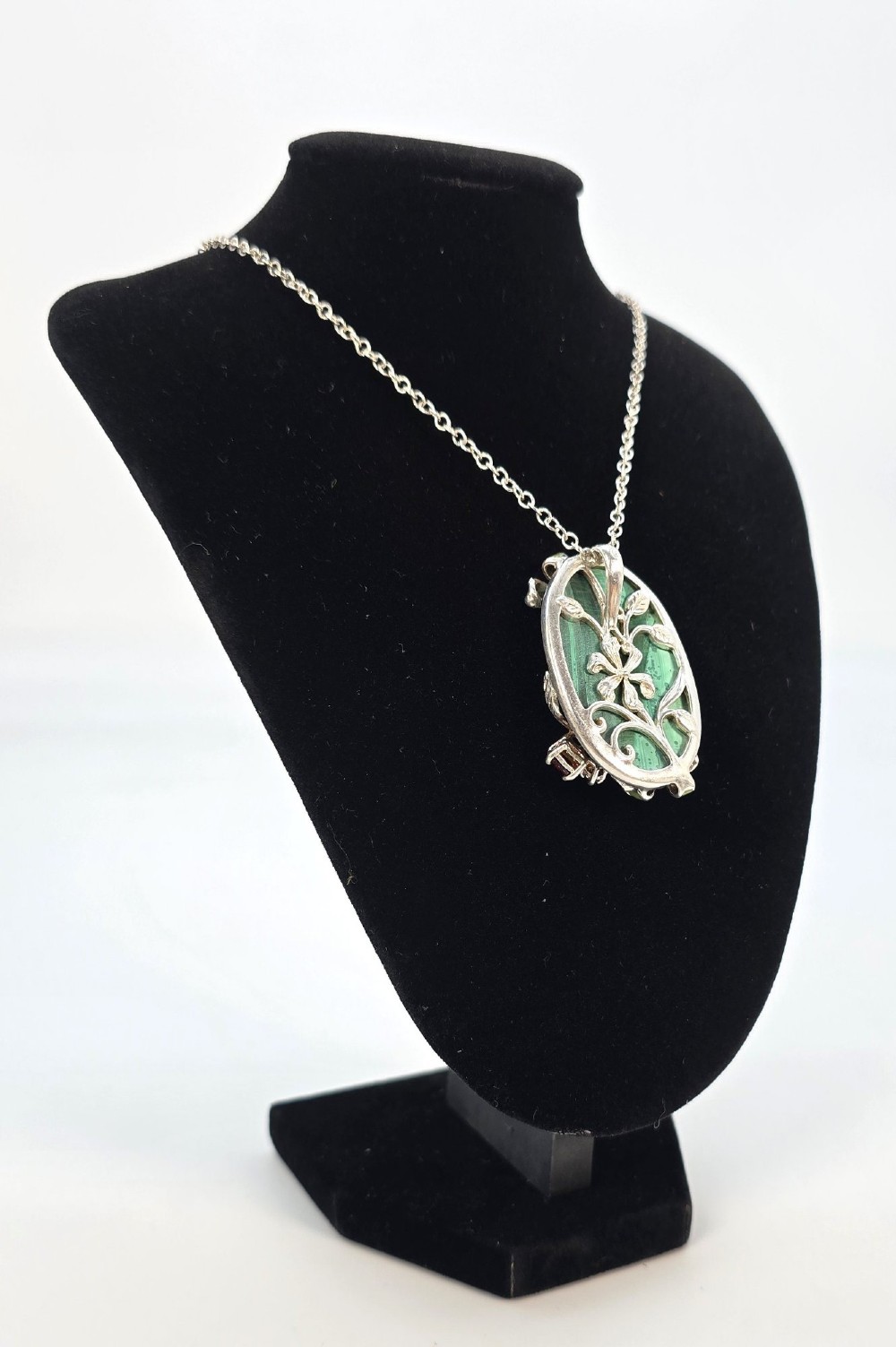 An oval green malachite pendant framed in silver metalwork with enamelled floral motifs, attached to a silver chain. View IV