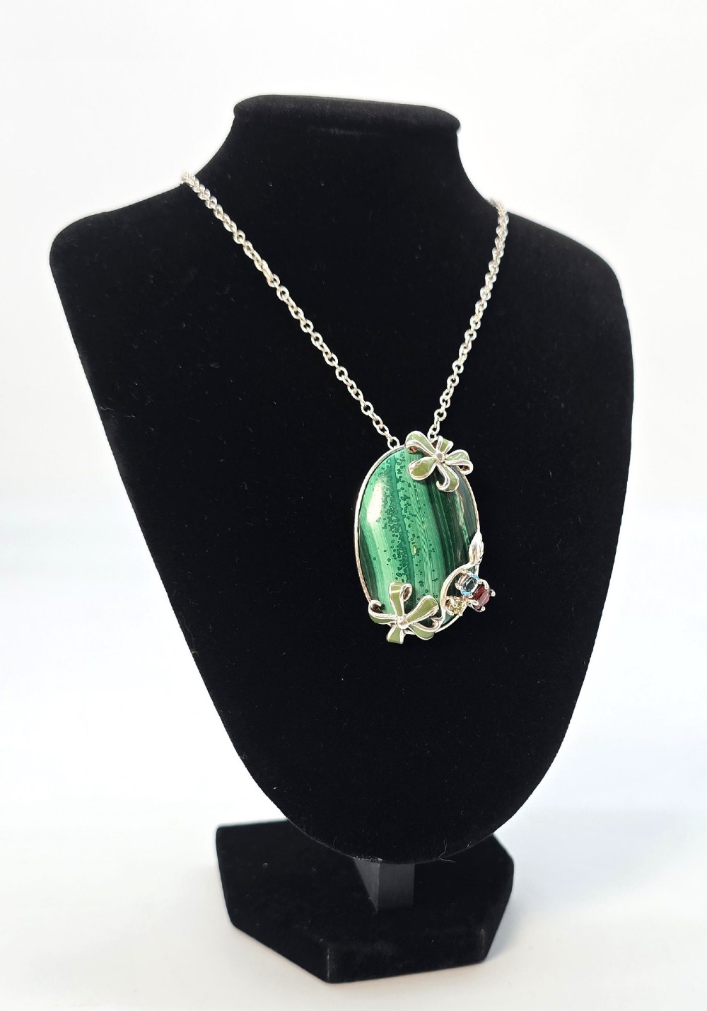 An oval green malachite pendant framed in silver metalwork with enamelled floral motifs, attached to a silver chain. View VIII