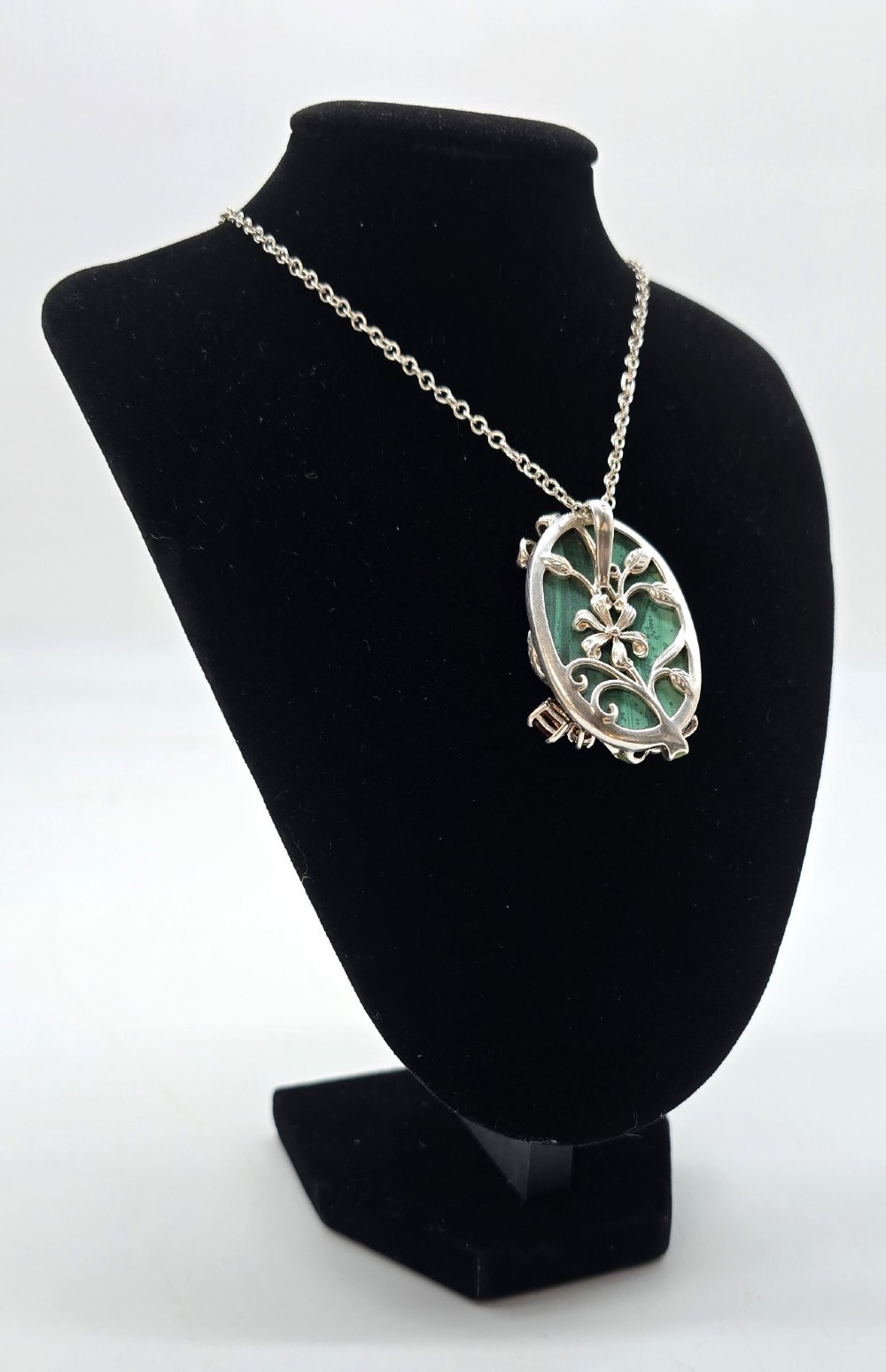 An oval green malachite pendant framed in silver metalwork with enamelled floral motifs, attached to a silver chain. View XI