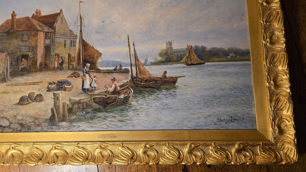An antique oil painting depicting a coastal harbour scene with boats and figures, set within an ornate carved gold frame. View II