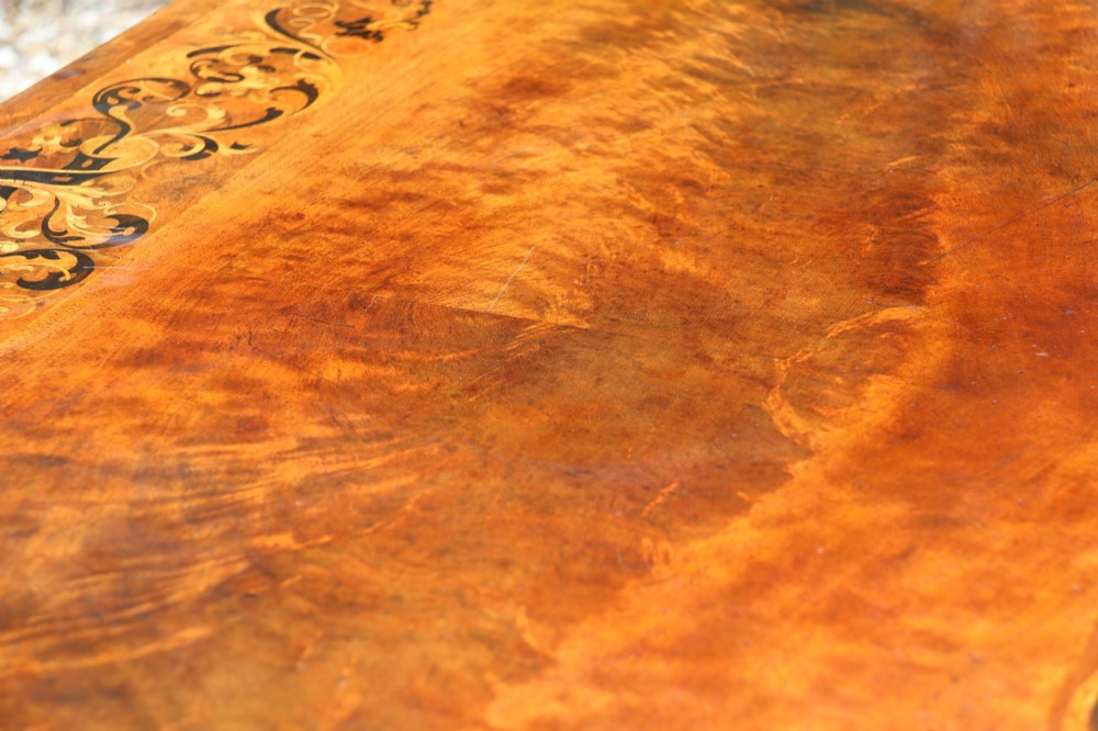 An early 19th-century flame mahogany library table featuring floral marquetry inlays around the rectangular top, frieze drawers with brass handles, and carved trestle supports. View V