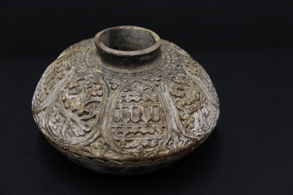 A squat rounded 17th-century Indian earthenware vase featuring deeply incised floral motifs and a low flared neck. View II