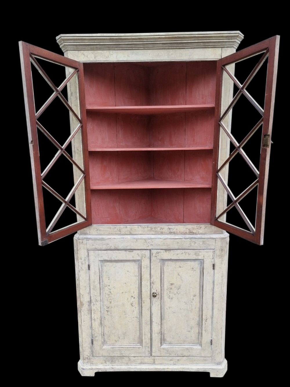 An antique two-part painted corner cupboard featuring an upper section with diamond-latticed glass doors showing a red painted interior and a solid two-door lower cabinet. View II