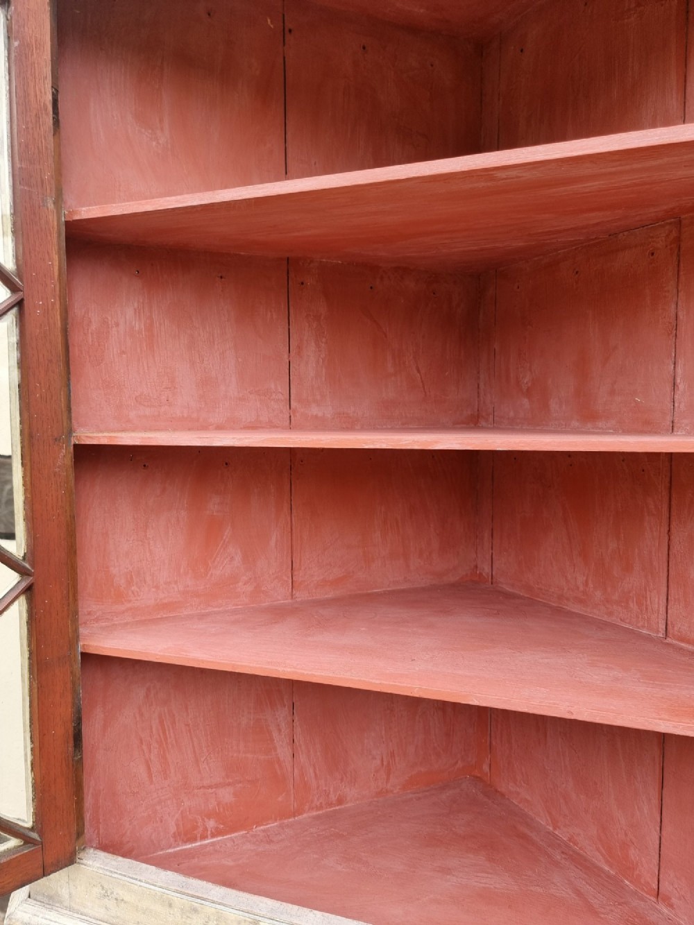 An antique two-part painted corner cupboard featuring an upper section with diamond-latticed glass doors showing a red painted interior and a solid two-door lower cabinet. View VI