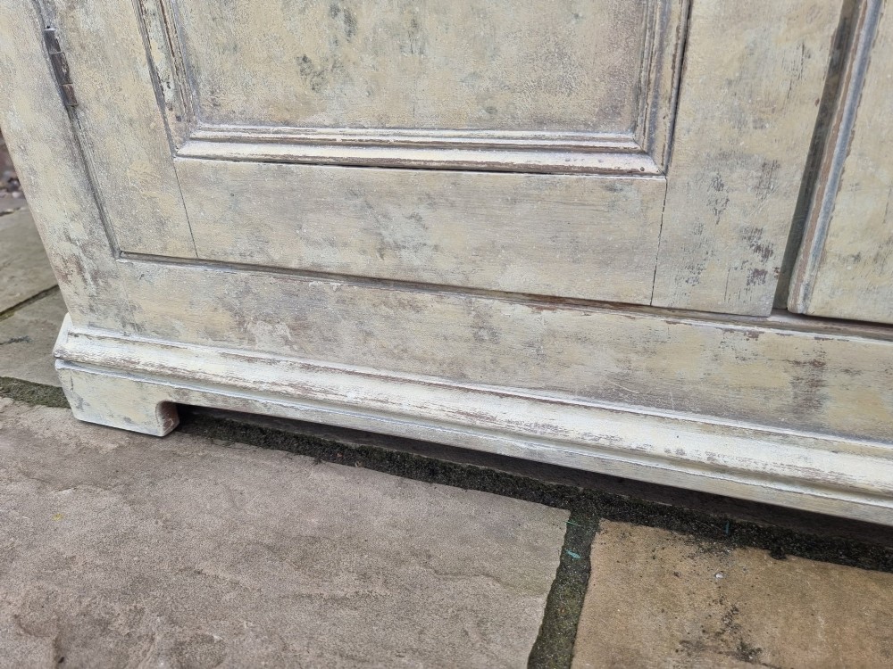 An antique two-part painted corner cupboard featuring an upper section with diamond-latticed glass doors showing a red painted interior and a solid two-door lower cabinet. View VII