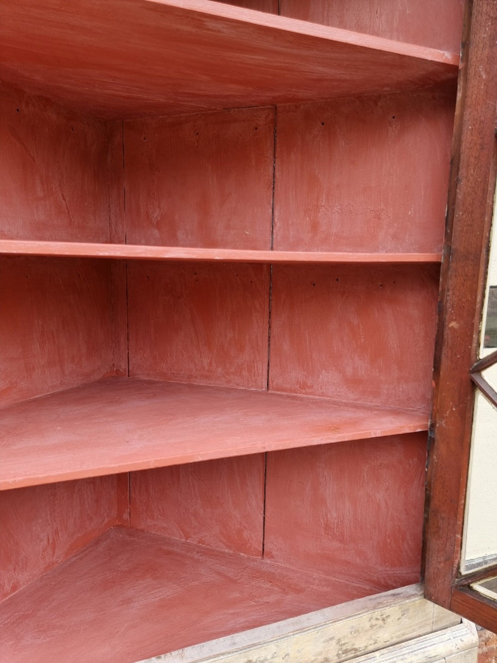 An antique two-part painted corner cupboard featuring an upper section with diamond-latticed glass doors showing a red painted interior and a solid two-door lower cabinet. View VIII