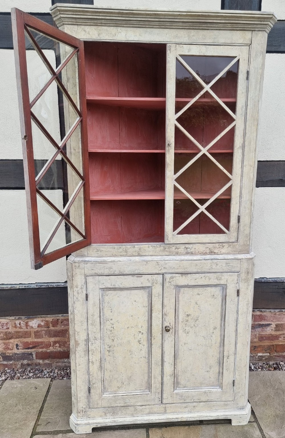 An antique two-part painted corner cupboard featuring an upper section with diamond-latticed glass doors showing a red painted interior and a solid two-door lower cabinet. View IX