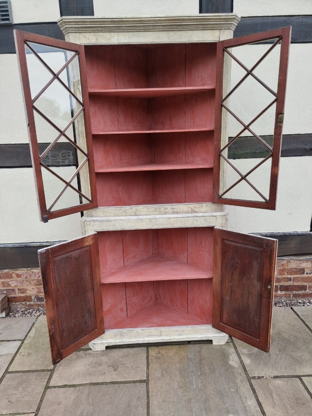 An antique two-part painted corner cupboard featuring an upper section with diamond-latticed glass doors showing a red painted interior and a solid two-door lower cabinet. View XII