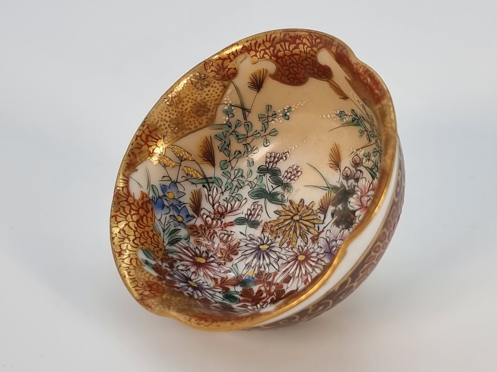 A pair of small, round Japanese porcelain bowls featuring intricate floral painted interiors and detailed red and gold geometric borders around scalloped rims. View III