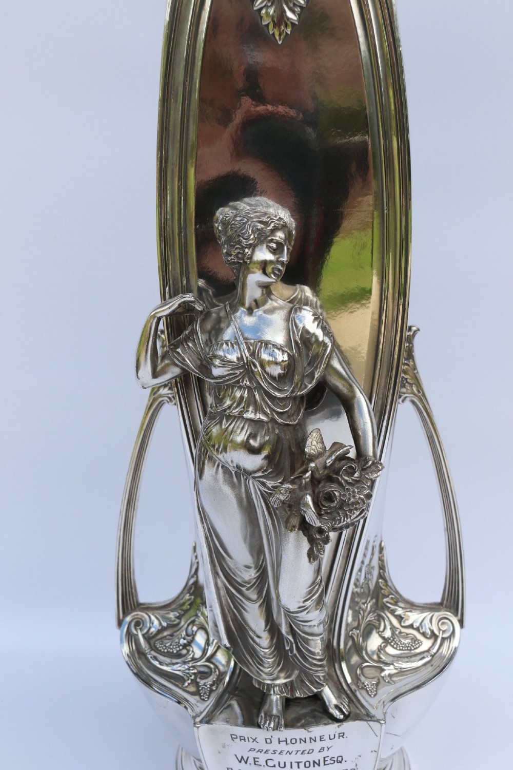 A tall silver-plated Art Nouveau vase featuring a relief figure of a maiden holding flowers, twin handles, an engraved presentation inscription at the base, and a clear glass liner. View IV