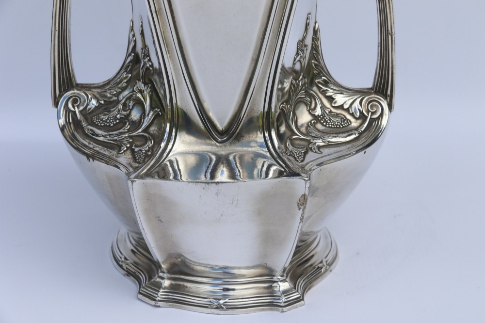 A tall silver-plated Art Nouveau vase featuring a relief figure of a maiden holding flowers, twin handles, an engraved presentation inscription at the base, and a clear glass liner. View IX