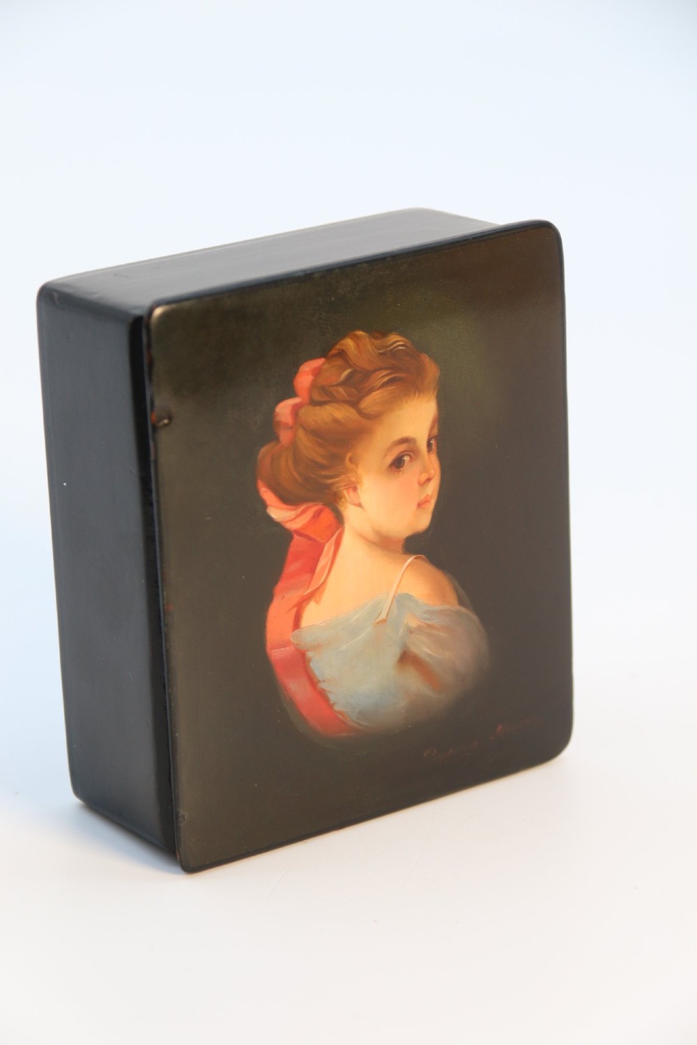 A rectangular black lacquered box featuring a hand-painted portrait of a young woman with a red ribbon in her hair on the top lid.