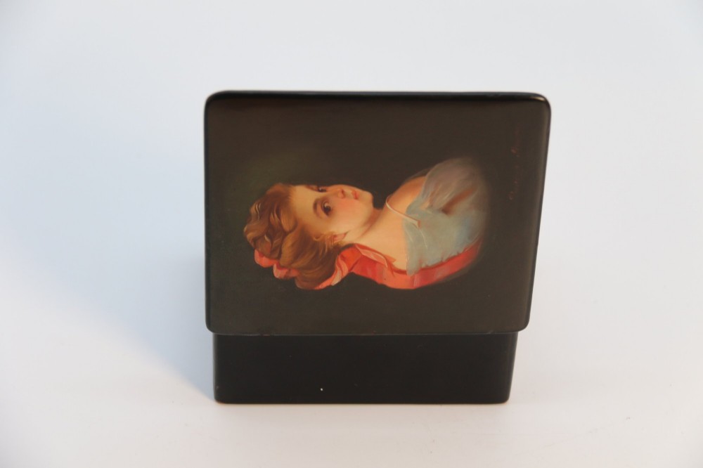 A rectangular black lacquered box featuring a hand-painted portrait of a young woman with a red ribbon in her hair on the top lid. View XII