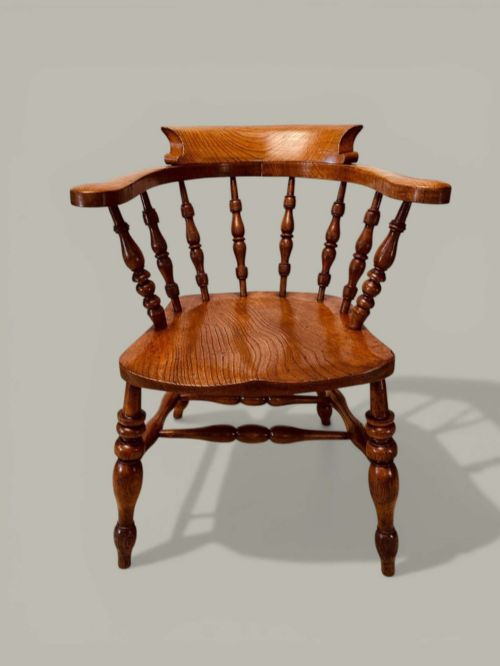 fig 1. A low-backed wooden Windsor armchair crafted from ash and elm with turned spindles, a curved horseshoe armrest, and a shaped saddle seat.