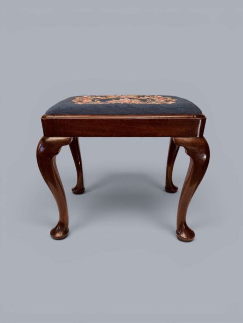 fig 1. A rectangular red walnut stool with carved cabriole legs, pad feet, and a navy blue needlepoint upholstered seat featuring a central floral wreath motif.