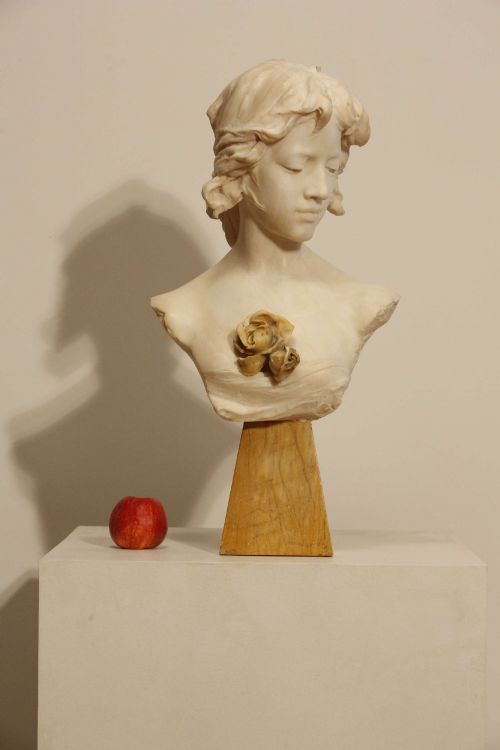fig 1. An early twentieth-century carved Carrara marble bust depicting a young female subject with a carved floral corsage, mounted on a wooden pedestal base.