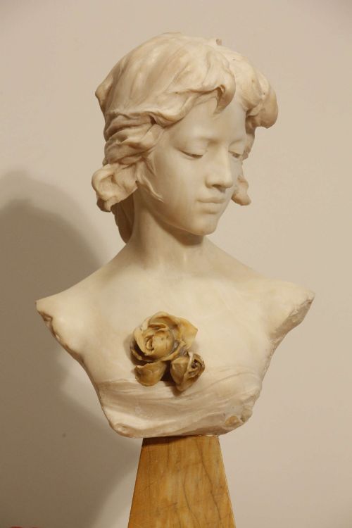 fig 2. An early twentieth-century carved Carrara marble bust depicting a young female subject with a carved floral corsage, mounted on a wooden pedestal base.