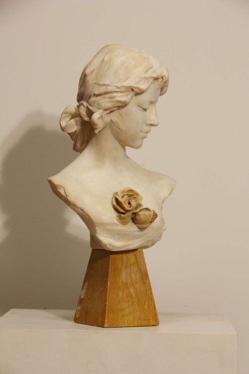 fig 4. An early twentieth-century carved Carrara marble bust depicting a young female subject with a carved floral corsage, mounted on a wooden pedestal base.