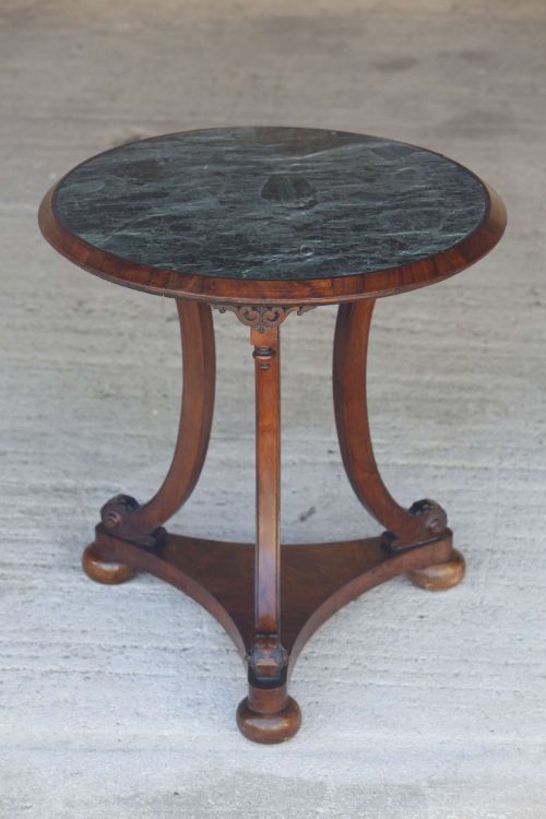 fig 1. A circular 19th-century French gueridon table featuring a dark green marble top supported by three curved mahogany legs resting on a shaped triform base.