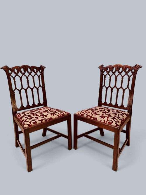 fig 1. A pair of mahogany side chairs featuring pierced Gothic tracery backrests, straight square legs with H-stretchers, and patterned red fabric upholstery.