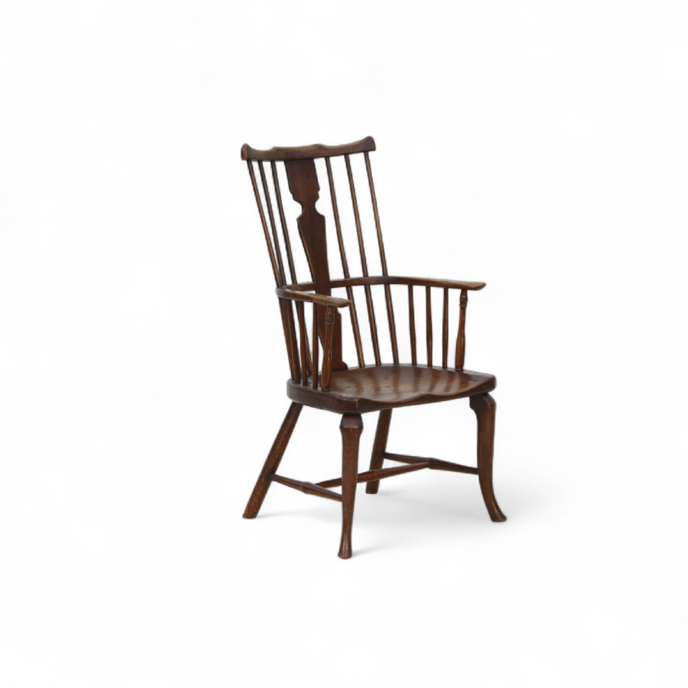 An 18th-century dark brown comb-back Windsor armchair made of ash and elm, featuring a high spindle back, central shaped splat, curved arms, and turned legs.