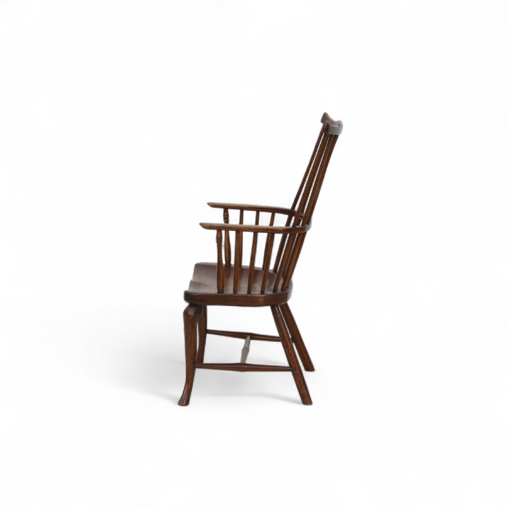 An 18th-century dark brown comb-back Windsor armchair made of ash and elm, featuring a high spindle back, central shaped splat, curved arms, and turned legs. View II