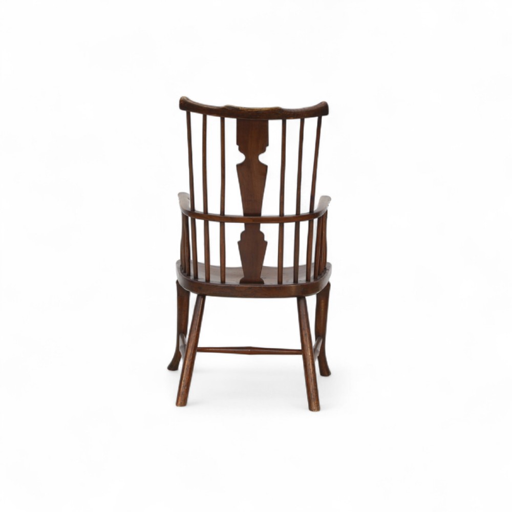 An 18th-century dark brown comb-back Windsor armchair made of ash and elm, featuring a high spindle back, central shaped splat, curved arms, and turned legs. View III