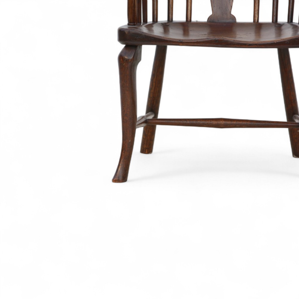 An 18th-century dark brown comb-back Windsor armchair made of ash and elm, featuring a high spindle back, central shaped splat, curved arms, and turned legs. View V