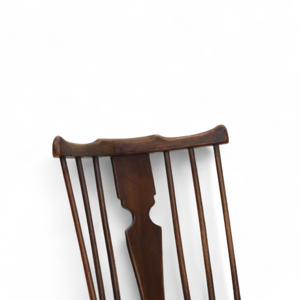 An 18th-century dark brown comb-back Windsor armchair made of ash and elm, featuring a high spindle back, central shaped splat, curved arms, and turned legs. View VI