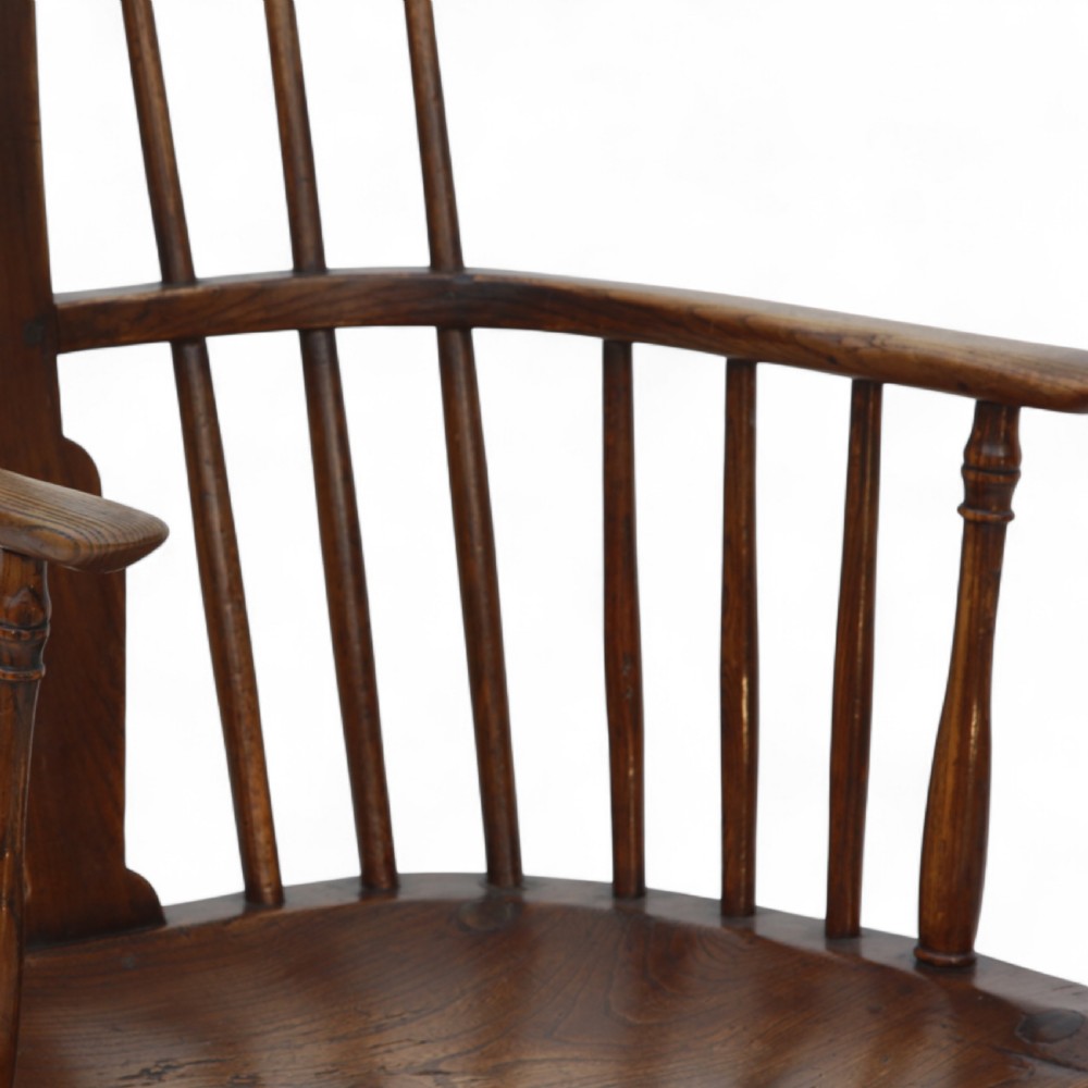 An 18th-century dark brown comb-back Windsor armchair made of ash and elm, featuring a high spindle back, central shaped splat, curved arms, and turned legs. View VII