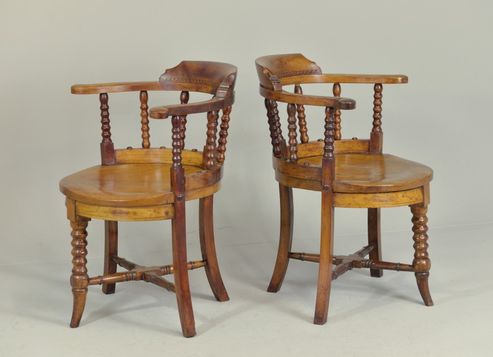 A set of six Victorian wooden captains armchairs featuring low curved backs, spindle supports, round solid seats, and turned legs. View II