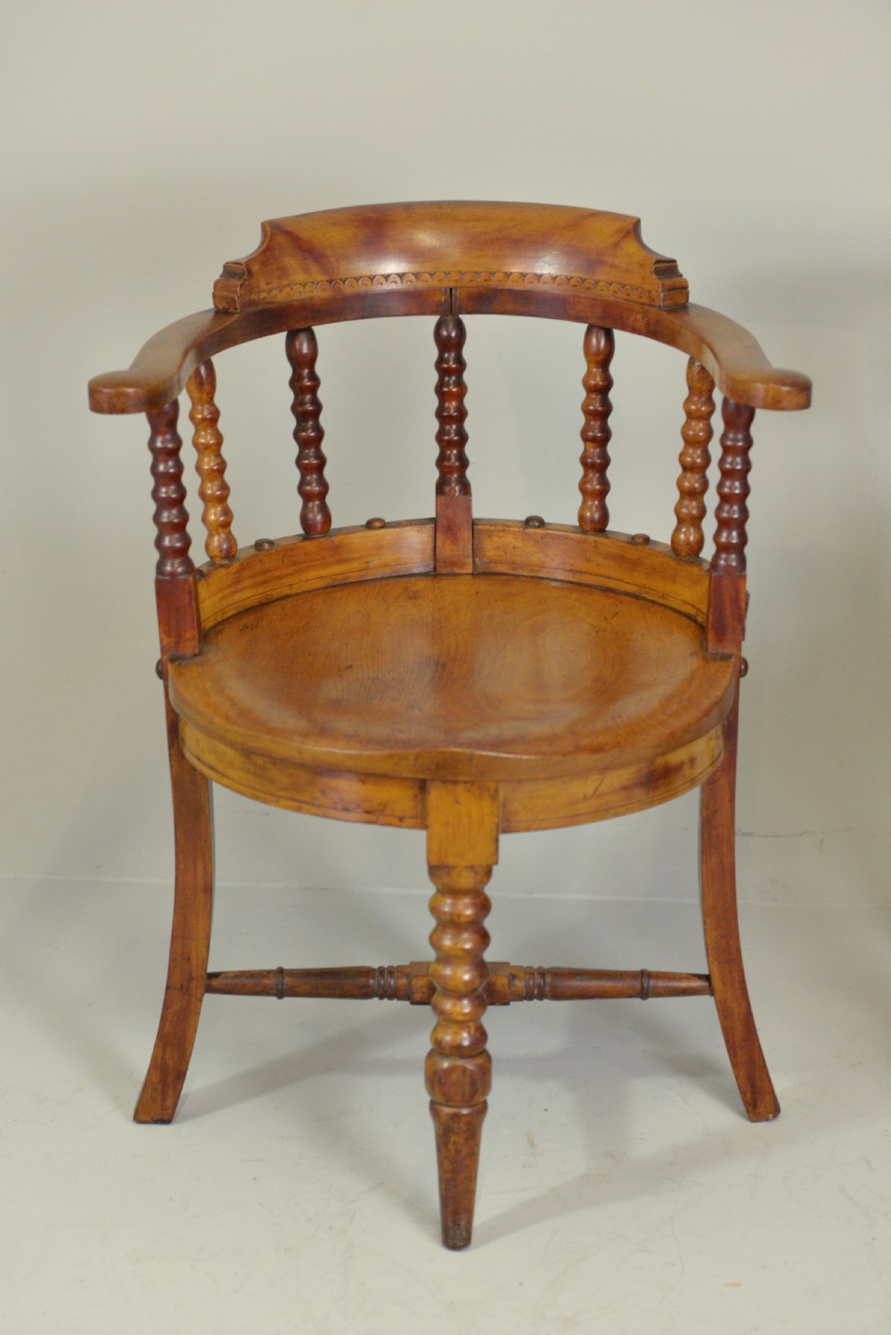 A set of six Victorian wooden captains armchairs featuring low curved backs, spindle supports, round solid seats, and turned legs. View III