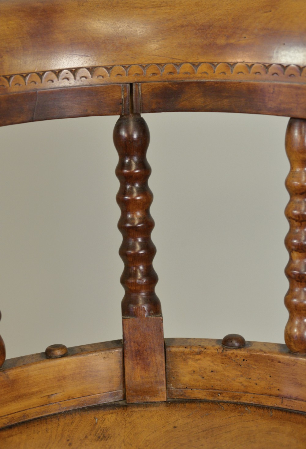 A set of six Victorian wooden captains armchairs featuring low curved backs, spindle supports, round solid seats, and turned legs. View V