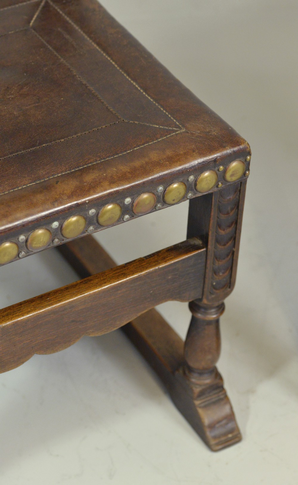 A pair of Victorian Spanish Revival oak dining chairs featuring brown leather seats, embossed back panels, and large brass stud detailing. View VI