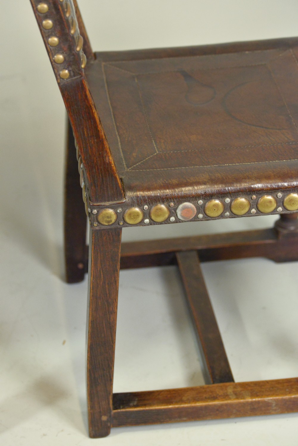 A pair of Victorian Spanish Revival oak dining chairs featuring brown leather seats, embossed back panels, and large brass stud detailing. View VIII