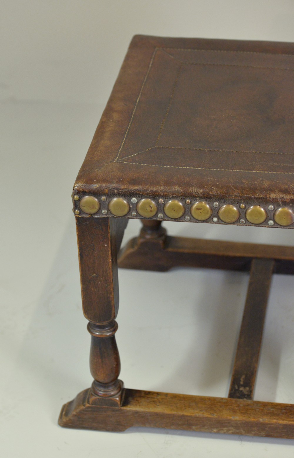 A pair of Victorian Spanish Revival oak dining chairs featuring brown leather seats, embossed back panels, and large brass stud detailing. View X