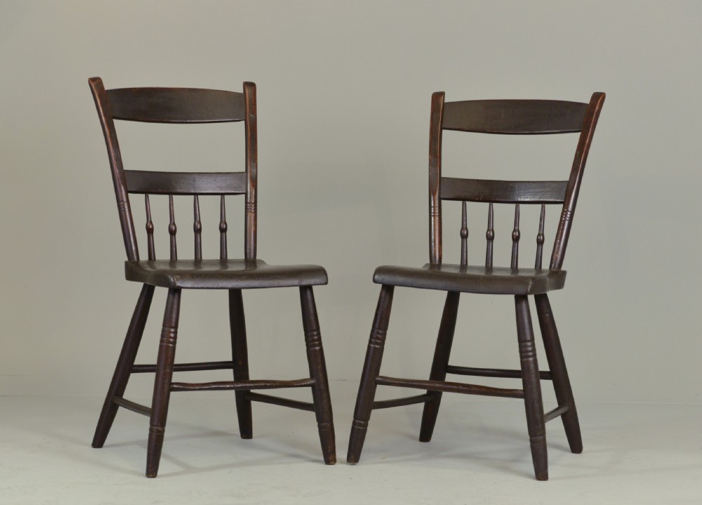 A pair of dark brown 19th-century American slat back wooden kitchen chairs featuring turned legs and back spindles.
