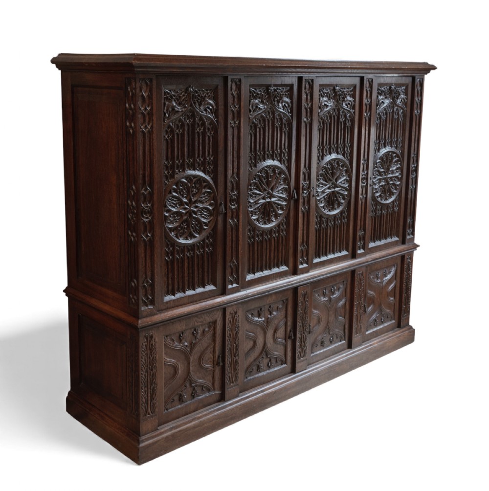 A large dark oak Gothic Revival cupboard featuring carved tracery panels, rose window motifs, and lower cabinet doors. View V