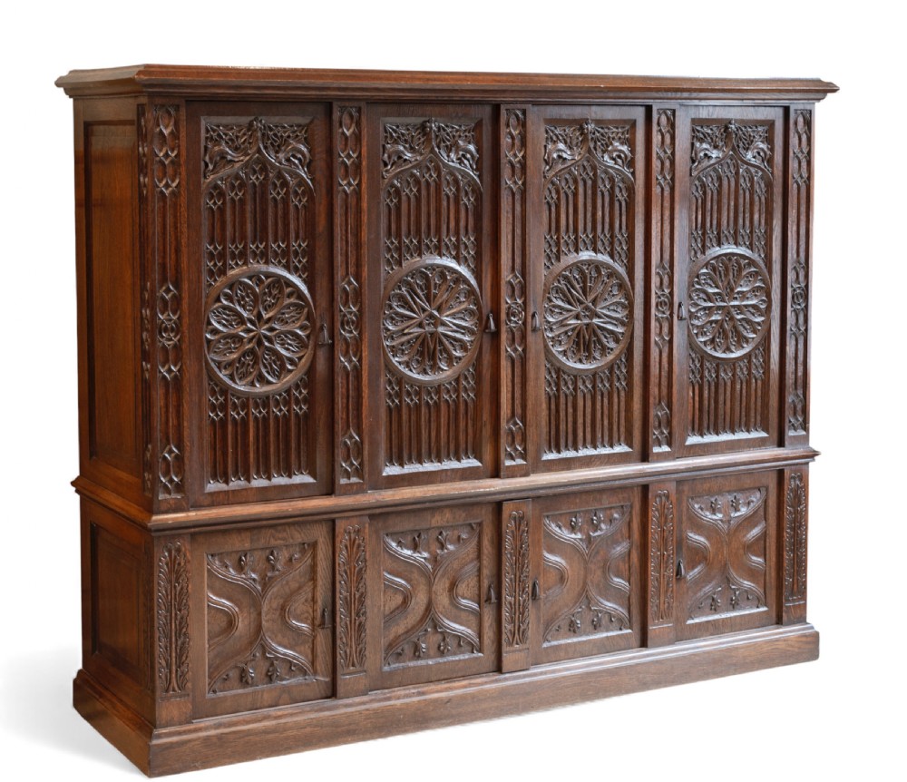 A large dark oak Gothic Revival cupboard featuring carved tracery panels, rose window motifs, and lower cabinet doors. View VIII